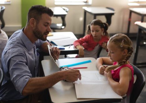 young-school-teacher-helping-girl-with-study-in-classroom-e1633425234264.jpg