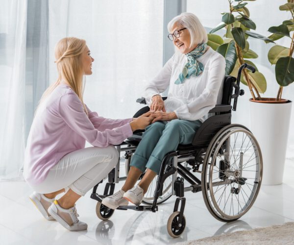 young-woman-speaking-with-senior-woman-in-wheelchair-at-nursing-home-e1632766549844.jpg